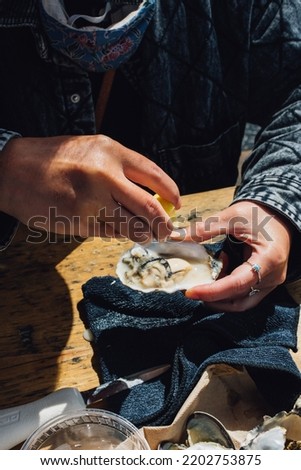woman shucking and eating oysters at outdoor restaurant  Royalty-Free Stock Photo #2202753875