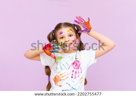 A little girl painted with multicolored paints will playfully have to create on a pink isolated background. Development of children's creativity for schoolchildren. Royalty-Free Stock Photo #2202755477
