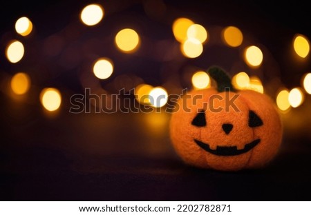 Halloween pumpkin on a dark bokeh lights background. Jack o Lantern head made of wool. Felting toy. Halloween greeting card. Copy space.