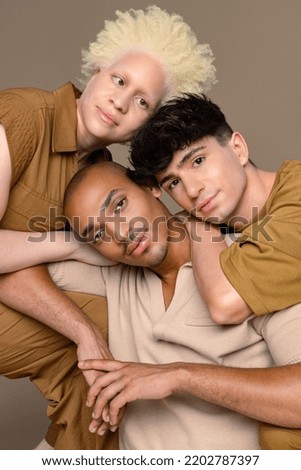 Studio shot of a non-binary Caucasian person in their 20's, a Black woman with albinism in her 20's, and a Hispanic man in his 20's posing together on a neutral background. Royalty-Free Stock Photo #2202787397