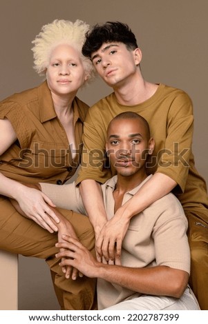 Portrait of a non-binary Caucasian person in their 20's, a Black woman with albinism in her 20's, and a Hispanic man in his 20's confidently looking at the camera on a neutral background. Royalty-Free Stock Photo #2202787399