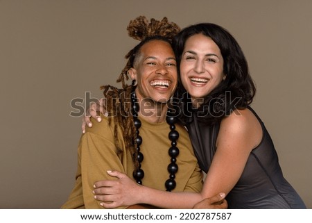 Close-up studio portrait of two beautiful models with diverse ethnicities posed smiling and embracing on a neutral background Royalty-Free Stock Photo #2202787587