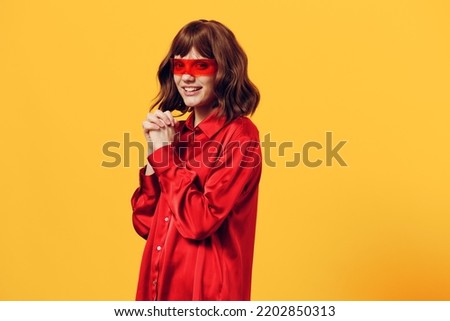 a sweet, happy woman stands in a stylish red shirt and red glasses on a yellow background, smiling broadly and posing in a relaxed pose. Horizontal Studio Photography
