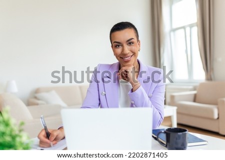 Remote job, technology and people concept - happy smiling young black business woman with laptop computer and papers working at home office