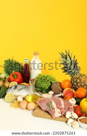 Group of different grocery on white table against yellow background