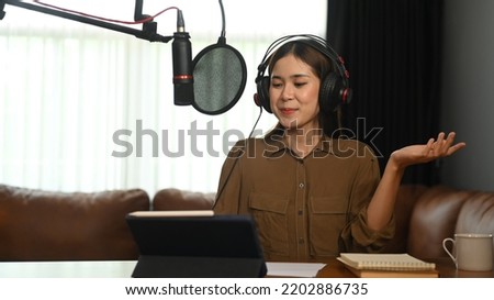 Smiling young woman using laptop and microphone streaming audio podcast at home studio