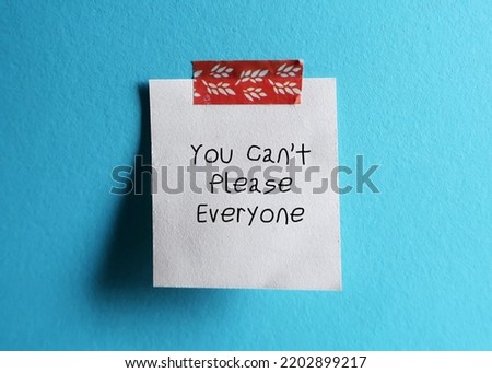 White note stick on blue background with handwritten text You Can’t Please Everyone - self reminder to stop trying to please everyone and be your authentic self Royalty-Free Stock Photo #2202899217