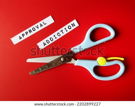 Scissors on blue background with text written paper pieces APPROVAL ADDICTION, refers to feeling insecure and unworthy of validation seeker, addicted to approval and validation from others Royalty-Free Stock Photo #2202899227