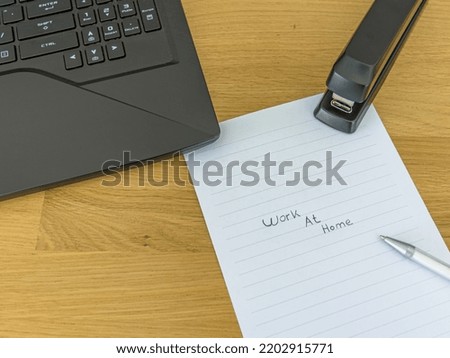 top view of a desk with a laptop, pen and stapler. On a piece of paper is the text "Work at home". Concept to indicate that you have to work from home during the covid pandemic 