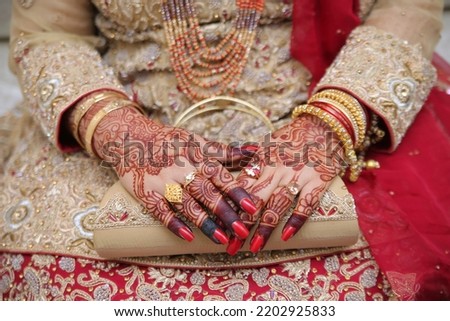 Bridal hands with mehndi, gold bangles and diamond rings, red nails and holding bridal clutch.