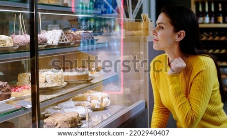 Taking details in the bakery cafe of a beautiful woman customer looking at the showcase fridge full of fresh deserts to choose the favourite one Royalty-Free Stock Photo #2202940407