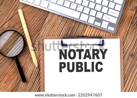 NOTARY PUBLIC text on paper clipboard with magnifier and keyboard on a wooden background