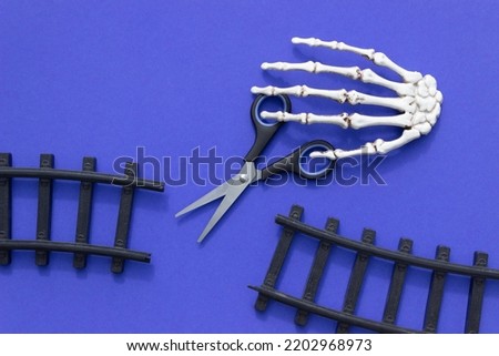 Two sections of a toy railway, scissors and a skeleton hand on a blue background. The end of the road