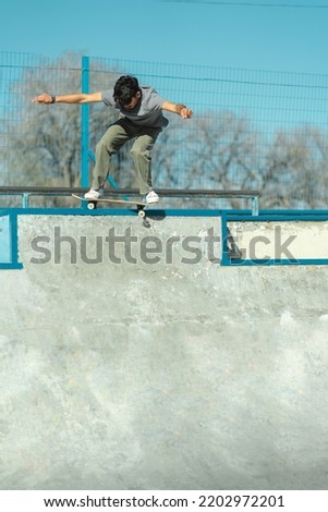 Skater boy riding his skateboard at the top of concrete bowl of skate park. Vertical photo. Copy Space