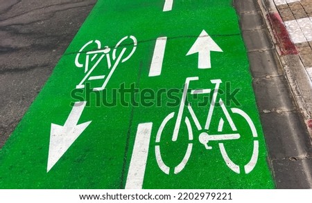 Green bicycle lane dedicated of separate for move cyclists on road in city. Arrows and bicycle symbol show movement in one and other directions. Sign on road ensures safety of people's lives.