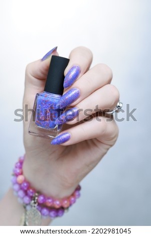Female hand with long nails and a bottle of lilac purple color nail polish