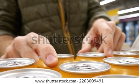 Close-up of many orange cans of beer and a male buyer's hands taking a couple