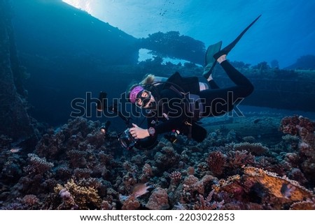 An underwater photographer looking at the camera taking pictures on the reef with a ship wreck in the background