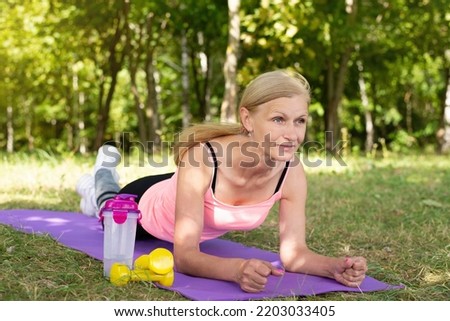 Sports in adulthood. A happy elderly woman does exercises, a photo of an older woman in the park in the fresh air, taking care of her health. Attractive older woman trains