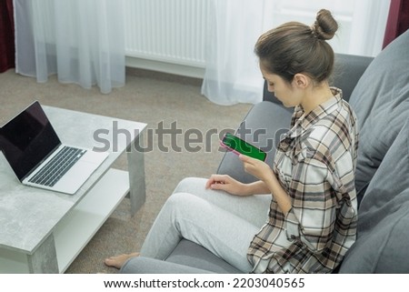 Side view of a girl at a laptop holding a phone in her hands. Modern work. Green screen. Generation Z.