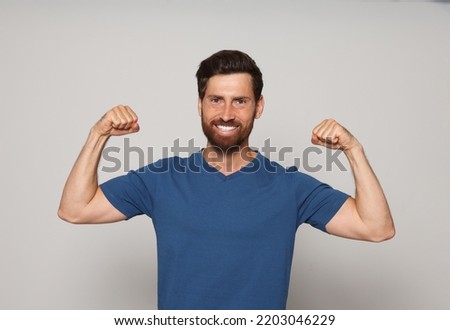 Smiling bearded man showing biceps on grey background