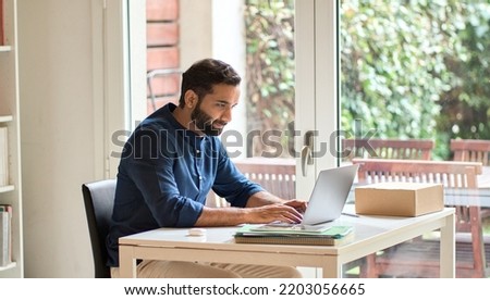 Indian ethnic business man, busy eastern male professional, serious businessman computing remote learning or distance working online typing on laptop using computer sitting at home office table. Royalty-Free Stock Photo #2203056665