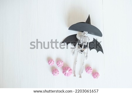 soft pink pumpkins on a light background and a toy skeleton in a witch hat , a place for text , an abstract Halloween concept