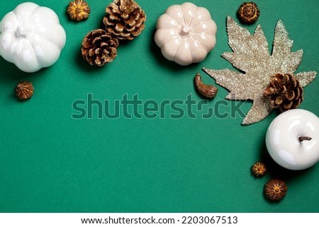 Autumn frame with white pumpkins and ceramic decor on dark green background. Fall card in white, green and gold colors, top view, copy space. Autumn season background