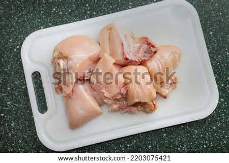 Top view of skinless chicken breasts with bone cut-up in half on top of a white plastic cutting board.