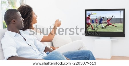 African american couple watching tv with football match on screen. Global sport concept, digital composite image.