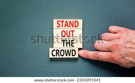 Stand out the crowd symbol. Concept words Stand out the crowd on wooden blocks on beautiful grey table grey background. Businessman hand. Business, stand out the crowd concept
