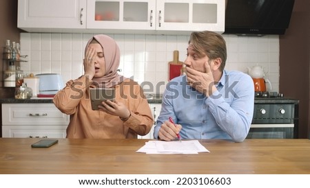 The man and his hijab-clad wife are calculating at the kitchen table. The couple discuss financial matters, calculate the payment status. Budget planning, controlling spending of money concept.