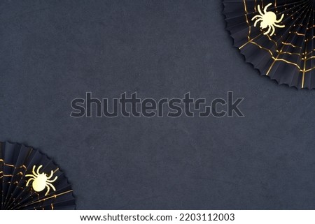 Black paper fans with golden cobwebs and golden glittering spiders on a dark background. The scary Halloween decoration on black with copy space. Halloween theme for your creativity.