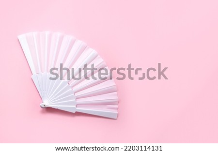 White fan on pink background. Minimal concept of menopause and female hot flashes. Copy space, top view