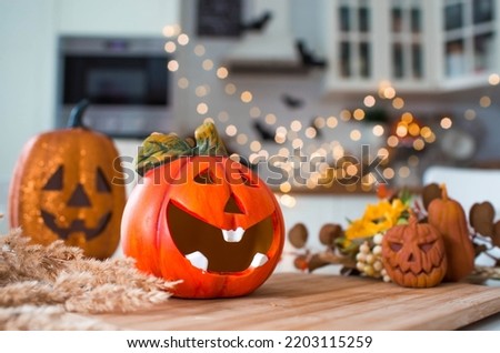 Autumn flowers, Jack's pumpkin and candles on a tray. In the background is the interior of a white Scandi-style kitchen. The concept of home and comfort. Autumn decor for Halloween.