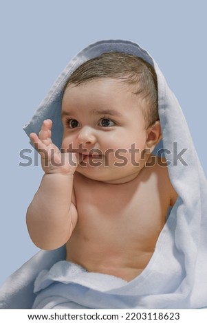 Cute baby sucking his finger covered in a blue towel with a blue background