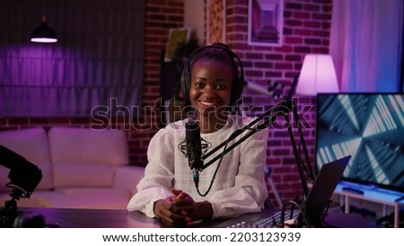 Portrait of african american podcaster sitting at desk in home recording studio with boom arm microphone and digital audio mixer. Online radio host smiling confident at camera while broadcasting live.