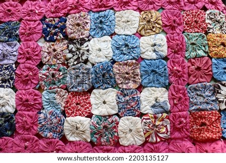 Vintage, multicolored yo-yo quilt, with rows of small yo-yo circles made of scraps of fabric carefully sewn together.  Quilt was made in a quilting circle during the Depression in North Carolina. Royalty-Free Stock Photo #2203135127