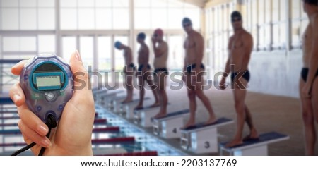 Close up of woman is holding a stopwatch on a white background against swimmers ready to plunge