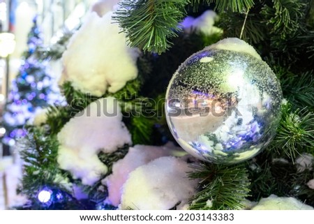 Closeup of Festively Decorated Outdoor Christmas tree with bright red balls on blurred sparkling fairy background. Defocused garland lights, Bokeh effect. The snowstorm.