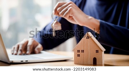 Businessman choosing mini wood house model from model and row of coin money on wood table, selective focus, Planning to buy property.
