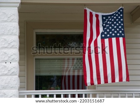 an American flag hangs on a white porch with its reflection in the house window
