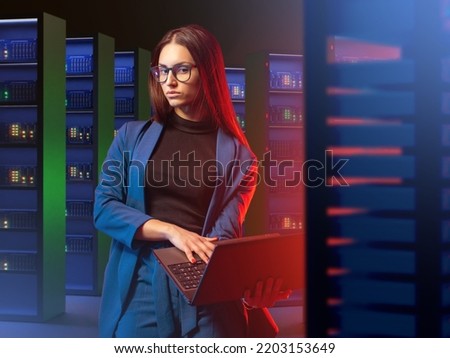 Employee of telecommunications company. Woman is standing with laptop. Girl in hosting providers room. Telecommunication business. Young woman looks into camera. Telecommunication equipment in racks