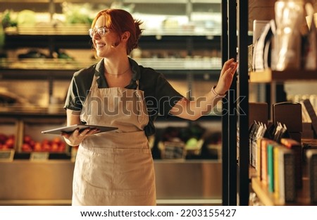 Successful shop owner smiling happily while holding a digital tablet in her grocery store. Cheerful female entrepreneur running a small business in the food industry.