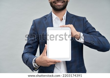 Smiling young business man professional manager, company employee, eastern businessman executive wearing suit holding digital tablet showing mockup screen template isolated on beige. Close up
