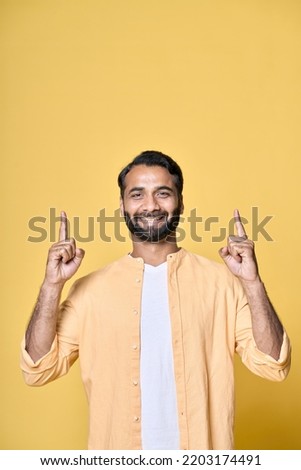 Happy indian man looking at camera pointing fingers up hand gesture indicating advertising new product commercial promotion, presenting sale offer standing isolated on yellow background. Vertical Royalty-Free Stock Photo #2203174491