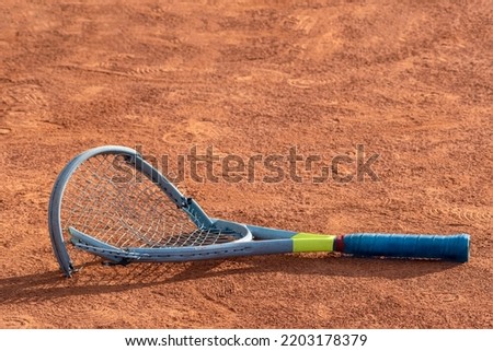 Broken tennis racket on clay tennis court. Mental health problem in sports. Negative emotions, stress, dissatisfaction, defeat, crash, failure, loss concept Royalty-Free Stock Photo #2203178379