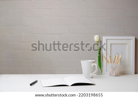 Home office desk with picture frame, coffee cup, tulip and notebook on white table. Copy space for your text.