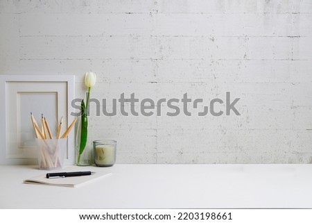 Feminine workplace with picture frame, candle and notebook on white table. Copy space for your text.