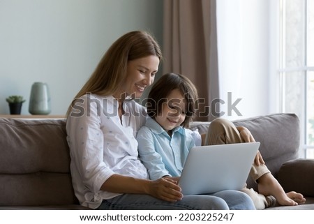 Happy pretty mom and curious son kid watching cartoon movie on laptop, reading book online, talking on video call, using online learning app, enjoying leisure. Family, Internet communication concept